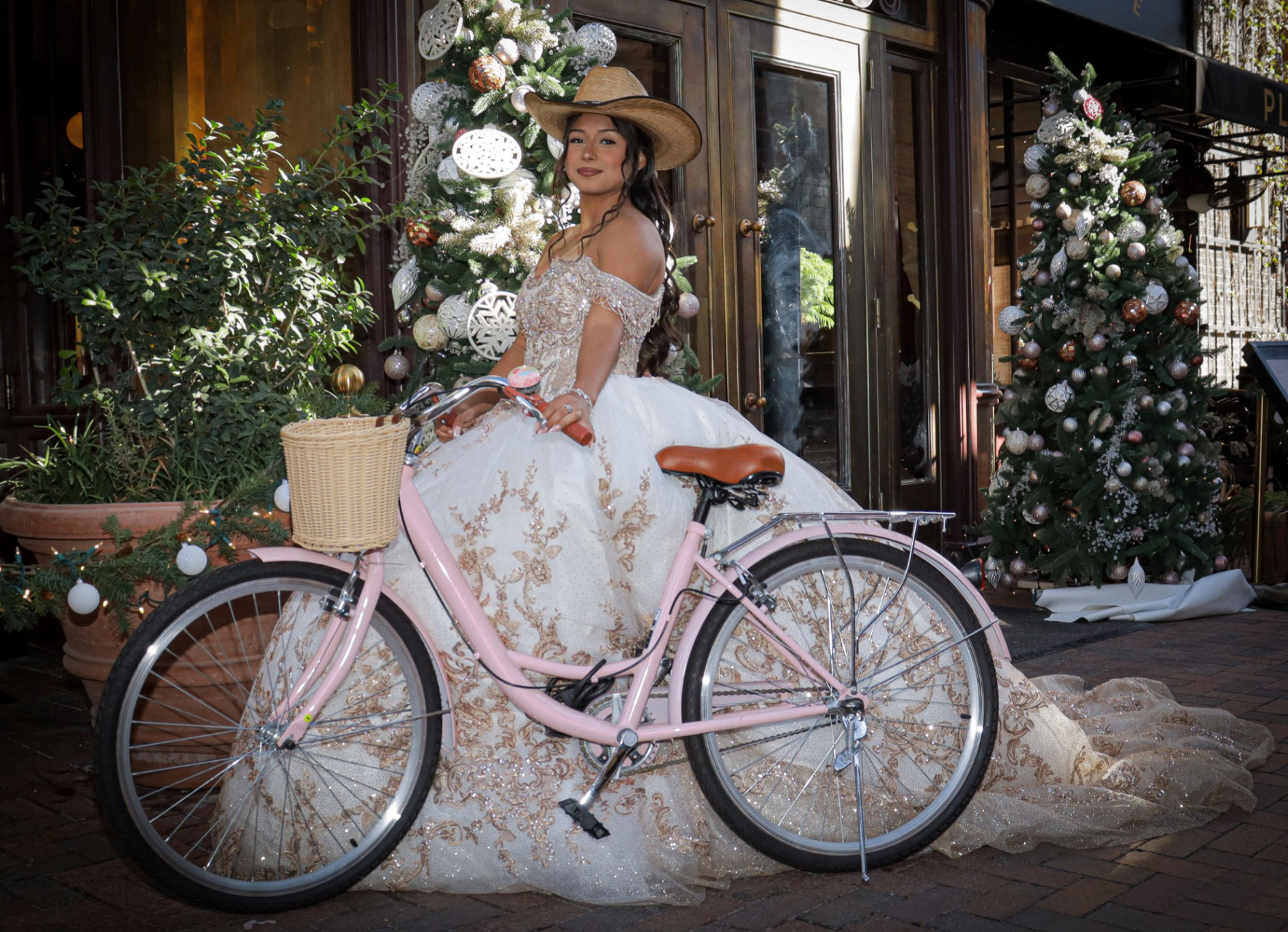 Quinceañera on a pink cruiser bike with cowboy hat at a holiday storefront